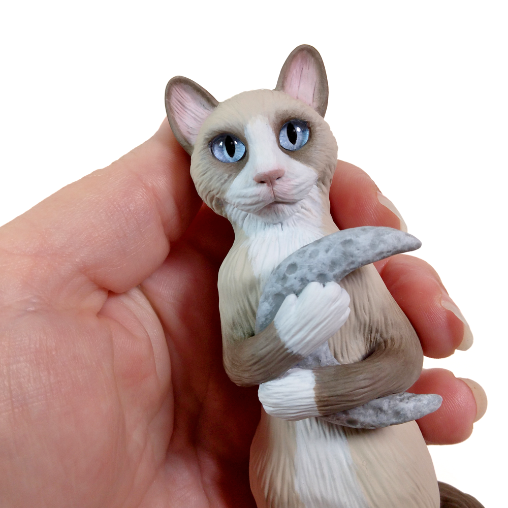 A polymer clay art figurine of a Snowshoe cat hugging a crescent moon. This hand-sculpted OOAK kitty has pale blue glass eyes that can penetrate your soul.